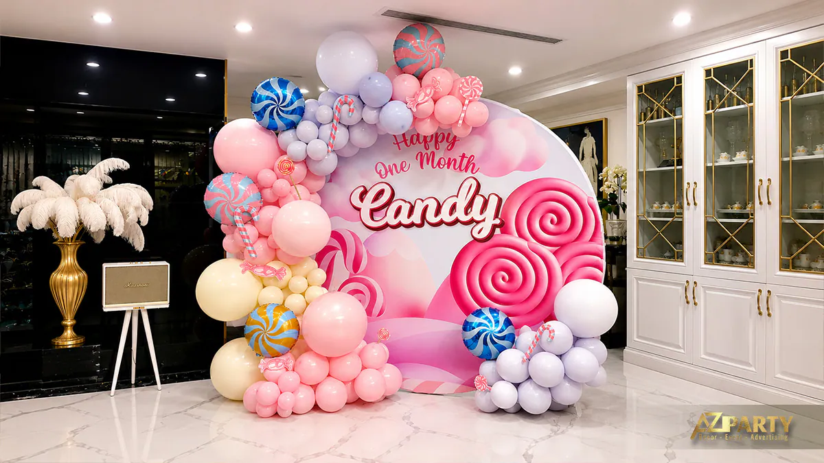 Toàn cảnh phông nền tiệc đầy tháng dễ thương của bé Candy đặt cạnh tủ kính trưng bày sang trọng trong nhà