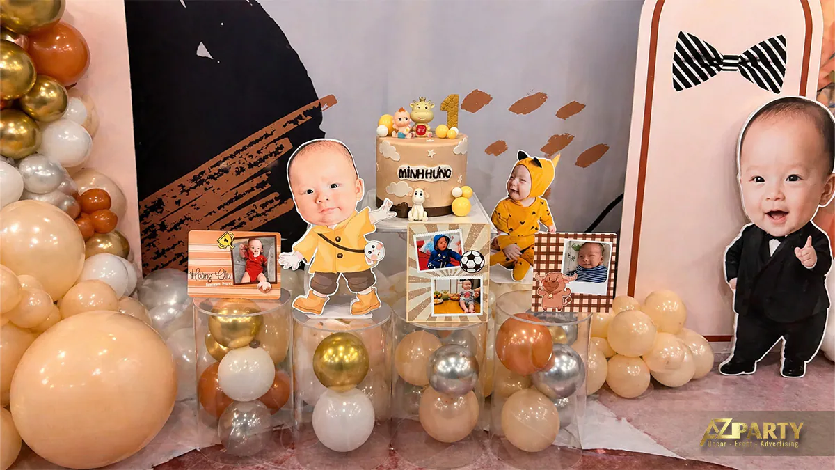 Bàn gallery tiệc thôi nôi bé Minh Hưng trưng bày chiếc bánh kem xinh xắn, các khung ảnh gia đình và hình chibi ngộ nghĩnh