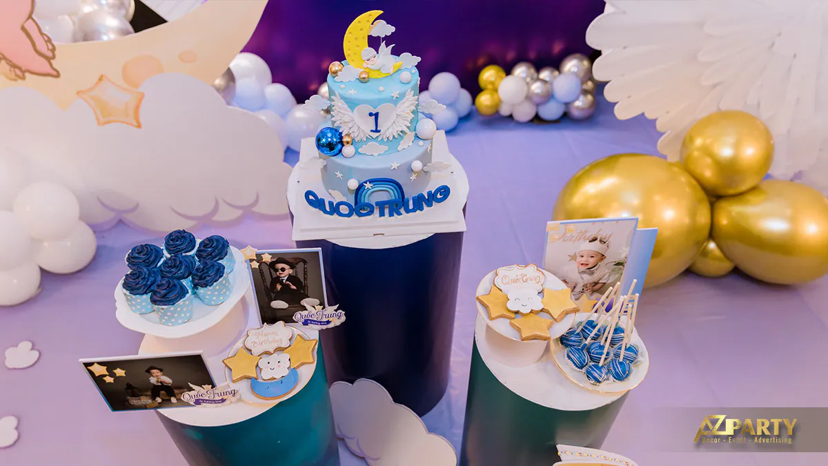 Bàn gallery tiệc thôi nôi bé Quốc Trung trưng bày bánh kem hai tầng màu xanh pastel cùng bánh cupcake và bánh quy hình ngôi sao xinh xắn