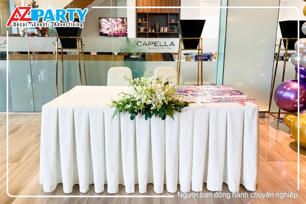 khu vực bàn tiếp tân được trang trí theo tone trắng, với hoa trên bàn, bên cạnh là hashtag để chụp hình