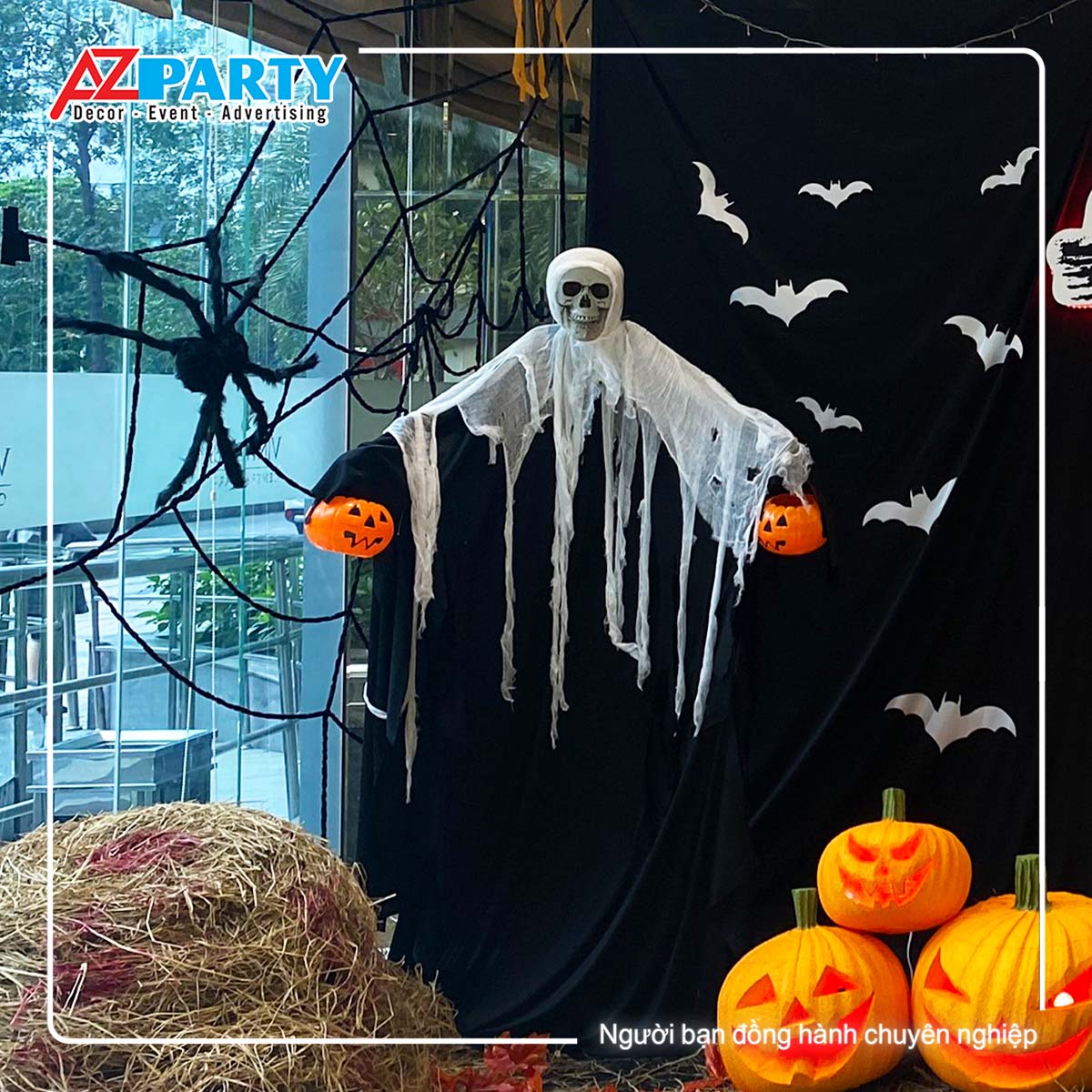 ma đen trùm vải trắng, trên tay có cầm những quả bí ngô, sau lưng là mạng nhện khổng lồ