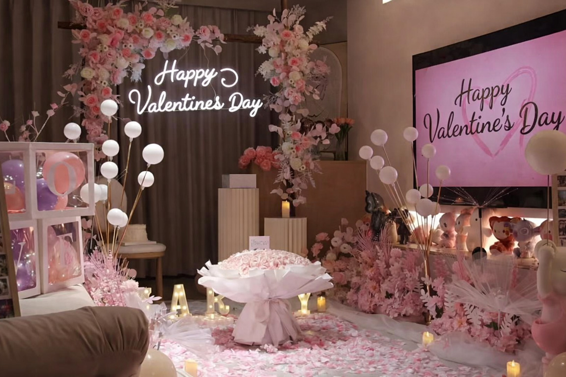 Trang trí Valentine tông hồng với backdrop hoa, đèn chữ Happy Valentine’s Day và không gian buổi tối lãng mạn trong nhà.