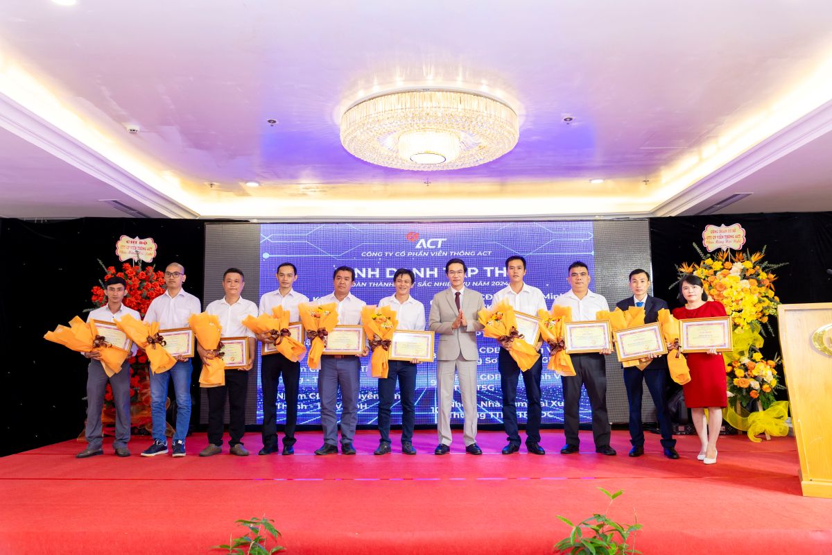 Tập thể các cá nhân và đại diện công ty chụp hình cùng hoa và bằng khen trên sân khấu