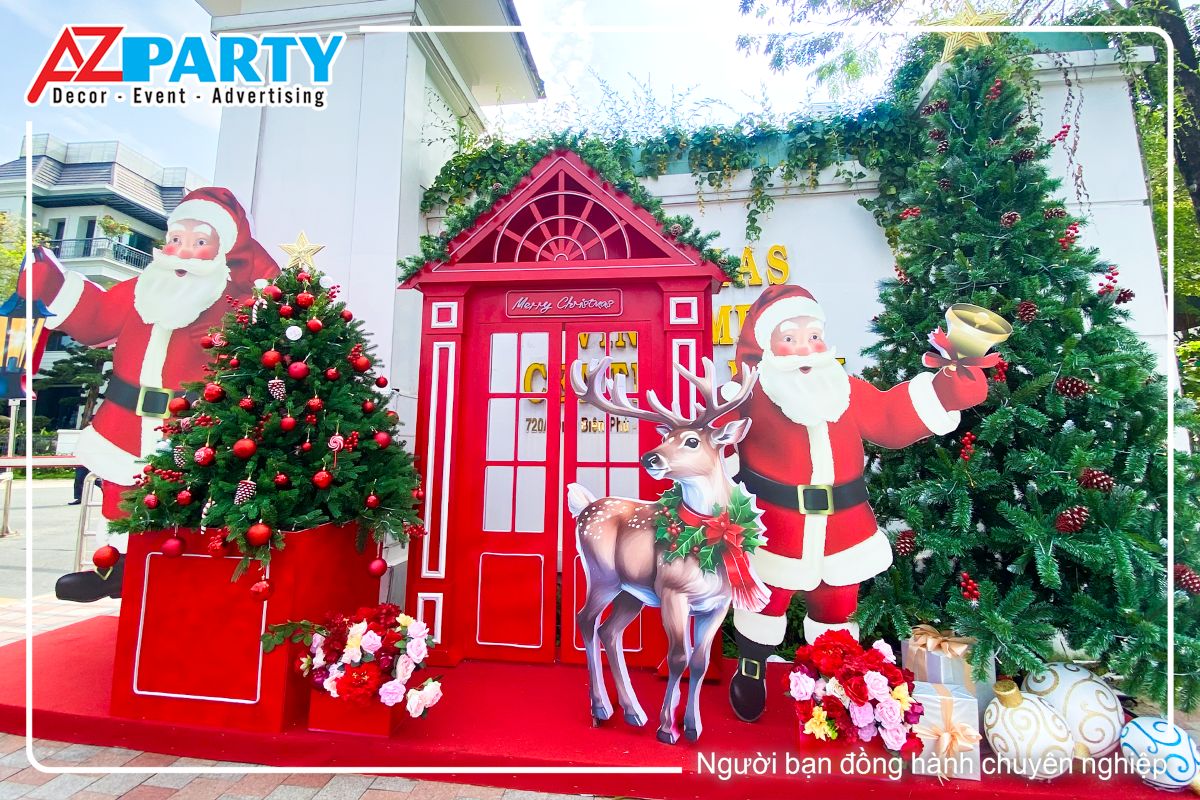 cận cảnh tiểu cảnh noel ông già noel cầm chiếc đèn cầy, ở giữa là mô hình phone booth, xung quanh là 2 cây thông xanh, ngoài cùng là ông già noel cầm chiếc chuông vàng cùng chú tuần lộc