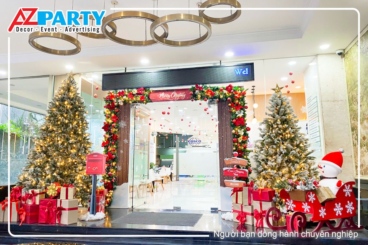 Tiểu cảnh noel trước cửa công ty Cosco, với 2 công ty lớn hai bên - rực rỡ, lung linh với ánh đèn vàng, dưới gốc cây là những hộp quà giáng sinh và chú người tuyết ngồi trên xe trượt tuyết, trước cửa vào được decor bằng dây thông