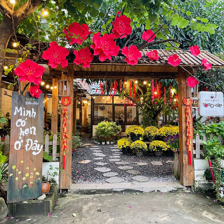 Cổng chào Tết trang trí hoa đỏ nổi bật, phên tre mộc mạc, đèn lồng và dây treo Tết 