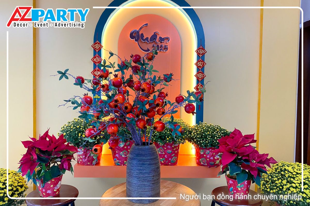 tiểu cảnh tết tại khu vực lầu trên của vietinbank, chính giữa là chậu cây lựu, 2 bên là 2 chậu hoa trạng nguyên cùng những chậu cúc mâm xôi, phía sau là dòng chữ xuân 2025