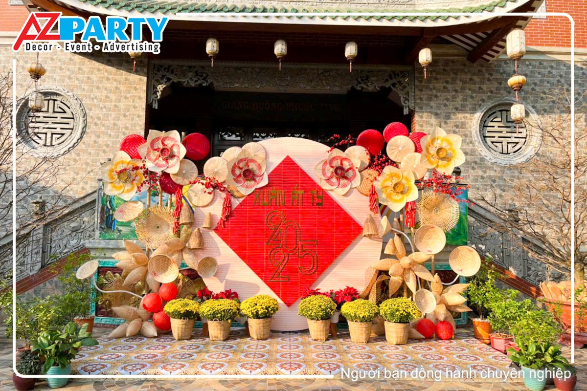 toàn cảnh tiểu cảnh tại chùa Vạn Đức năm 2025, tiểu cảnh sử dung các chất liệu từ tre lứa để trang trí với các sản phẩm như cái mẹt, nón lá, cái đó bắt cá. Chính giữa là backdrop hình tròn làm từ mành tre, ở giữa là dòng chữ Xuân Ất Tỵ 2025 vàng gold trên nên đỏ