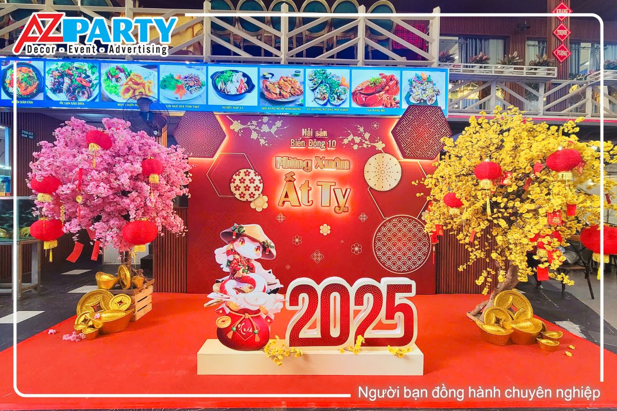 tiểu cảnh tết tại nhà hàng Biển Đông,2 bên tiểu cảnh là cây đào và cây mai vàng, ở giữa tiểu cảnh là dòng chữ 2025 nổi khối 3D túi tiền vàng và chú rấn linh vật